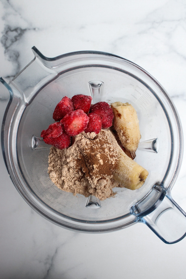 Frozen banana, frozen strawberries, vanilla protein powder, instant espresso, and cashew milk added to a blender.