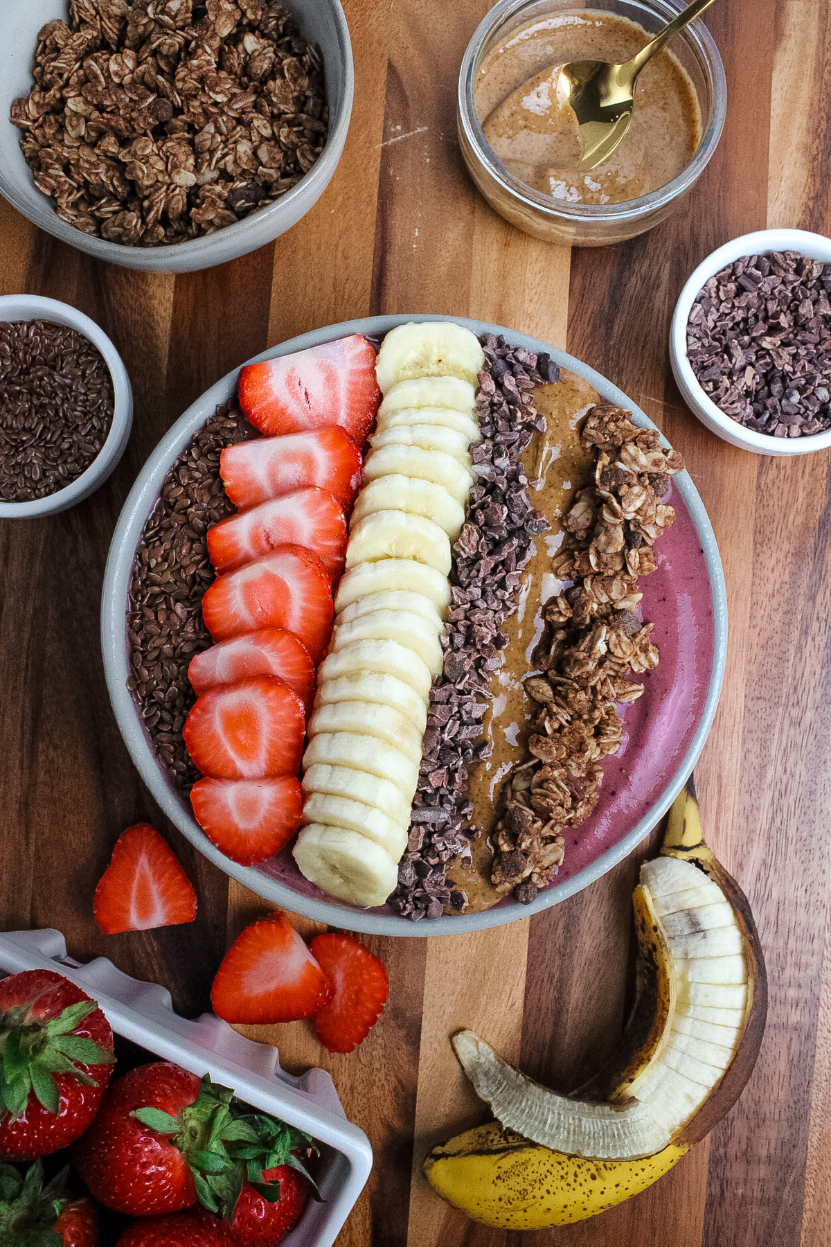 Finished strawberry banana espresso smoothie bowl topped with fruit, granola, almond butter, cacao nibs, and flaxseeds.