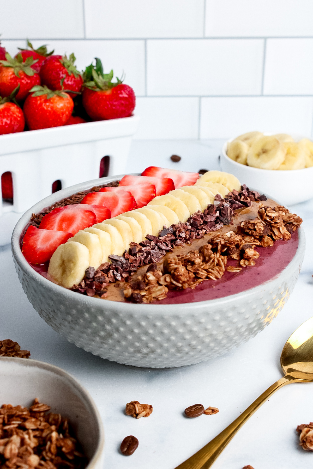 Low-angle view of a thick, creamy strawberry banana espresso smoothie bowl topped with fruit and granola.