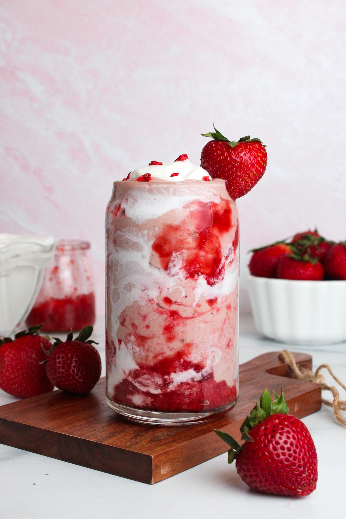 Strawberry glaze smoothie with coconut cream and strawberry swirls in a glass, garnished with a fresh strawberry.