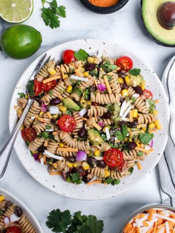 Vegan taco pasta salad with rotini, black beans, corn, avocado, tomatoes, red onion, cilantro, and dairy-free cheese on a plate.