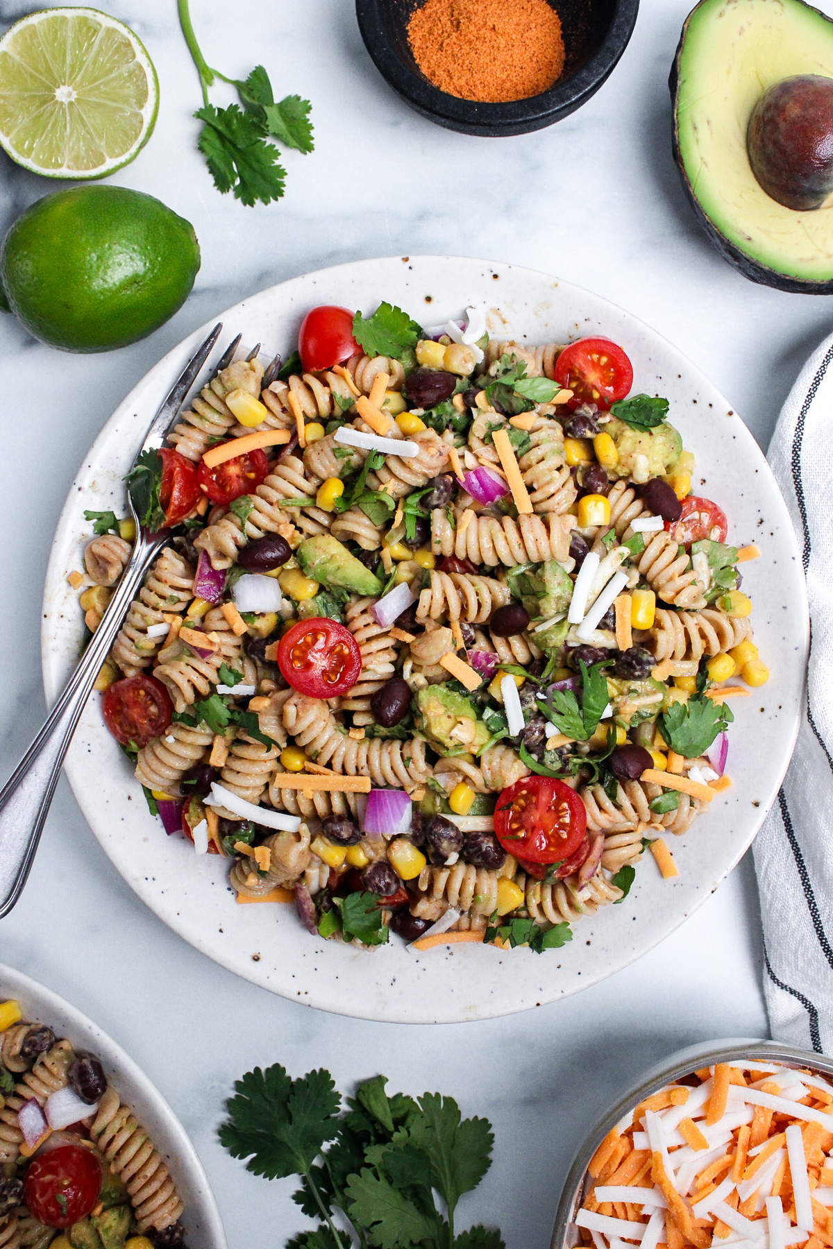 Vegan taco pasta salad with rotini, black beans, corn, avocado, tomatoes, red onion, cilantro, and dairy-free cheese on a plate with a fork.