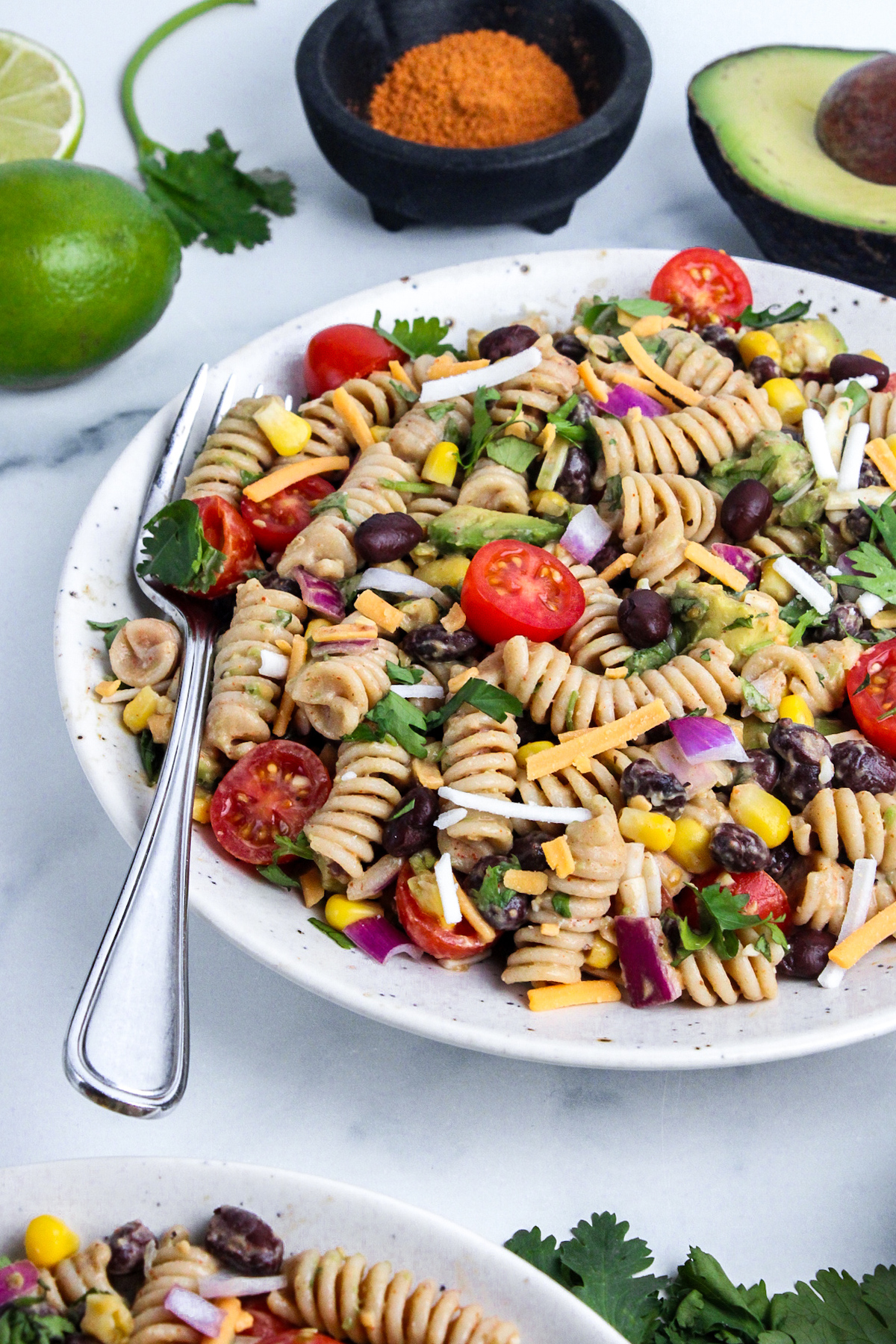 Angled view of vegan taco pasta salad with rotini, black beans, corn, avocado, tomatoes, red onion, cilantro, and creamy taco-seasoned dressing.