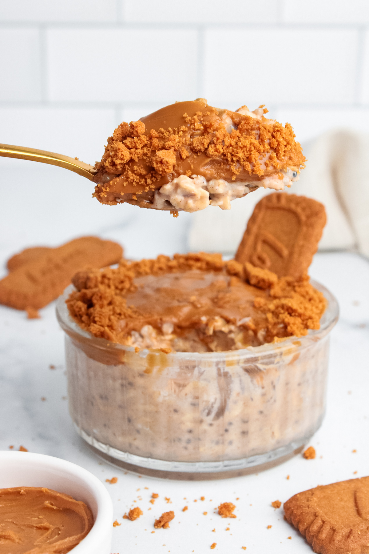 Biscoff overnight oats in a glass jar with a spoon taking a bite, showing the creamy texture and cookie butter topping.