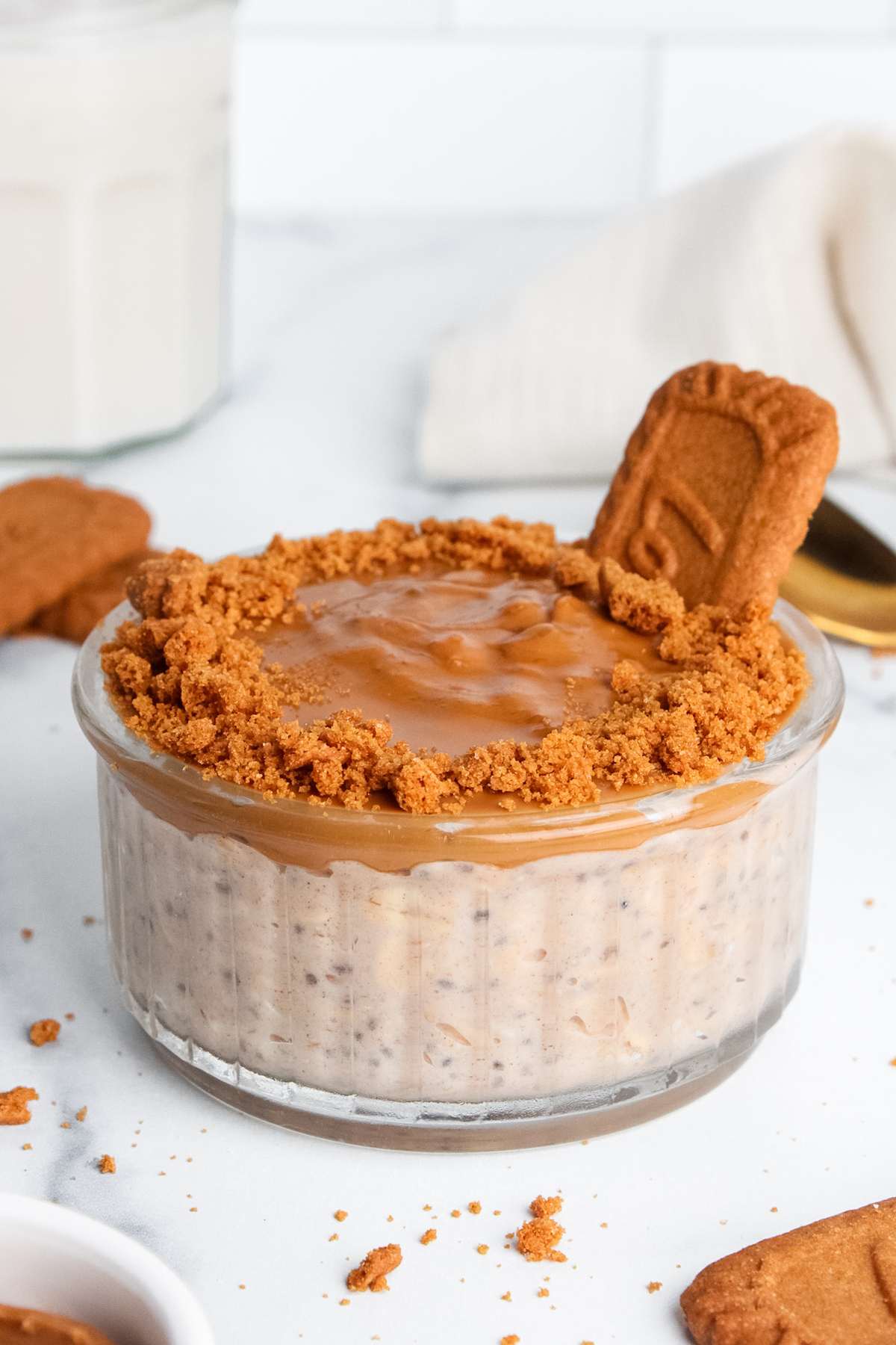 Creamy Biscoff overnight oats in a glass jar with a cookie butter layer, crushed Biscoff cookies around the rim, and a whole cookie on top.