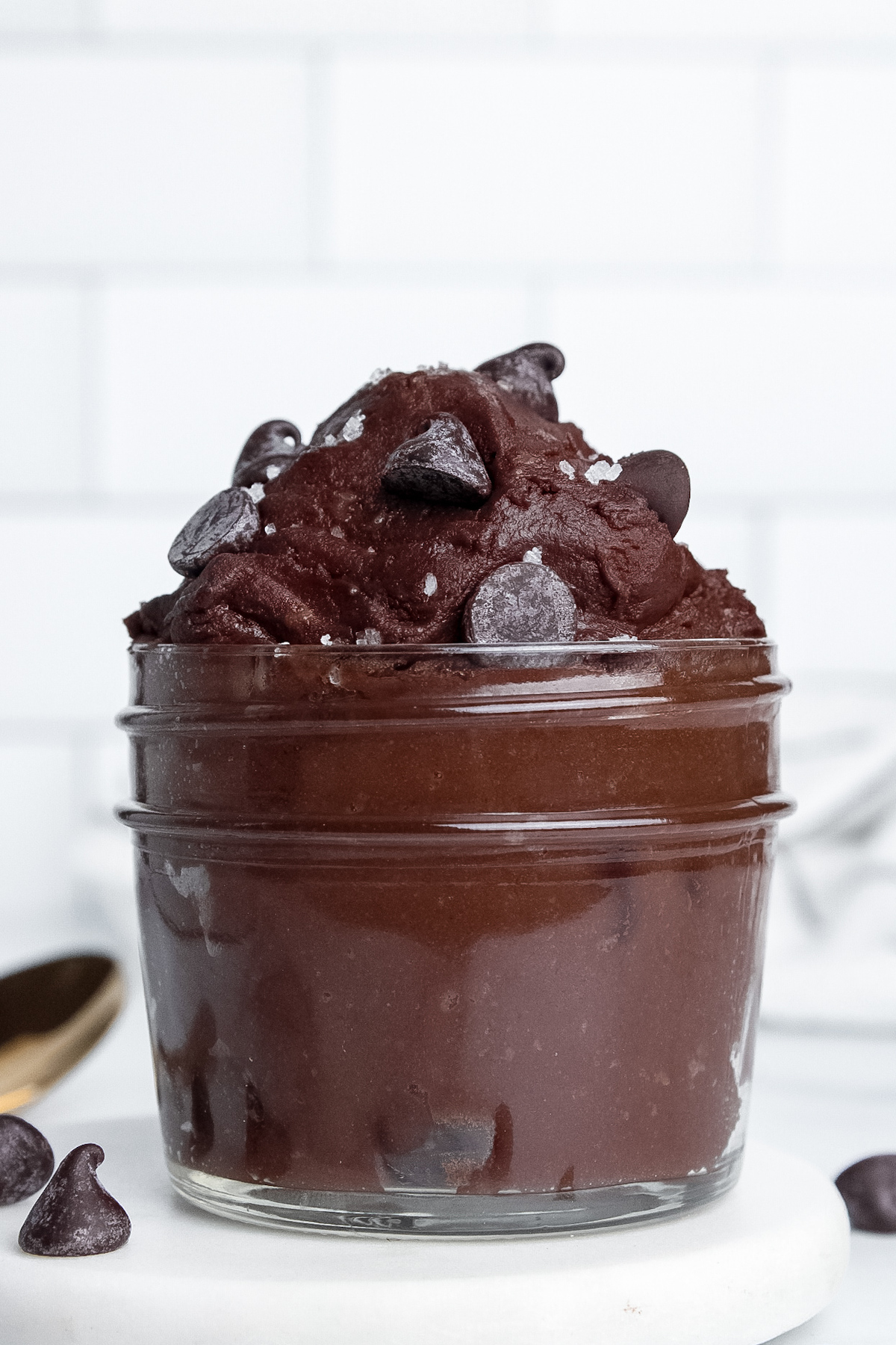 Straight-on view of a jar of single-serve protein brownie batter topped with chocolate chips and flaky sea salt.