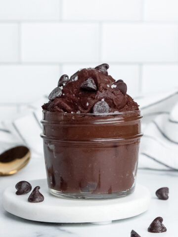 Single-serve vegan protein brownie batter in a jar, topped with chocolate chips and flaky sea salt.