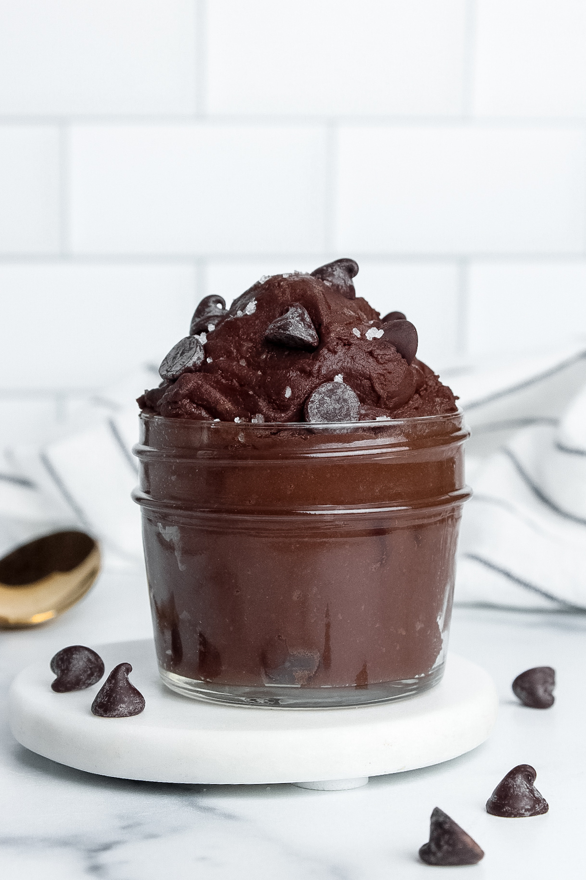 Single-serve vegan protein brownie batter in a jar, topped with chocolate chips and flaky sea salt.