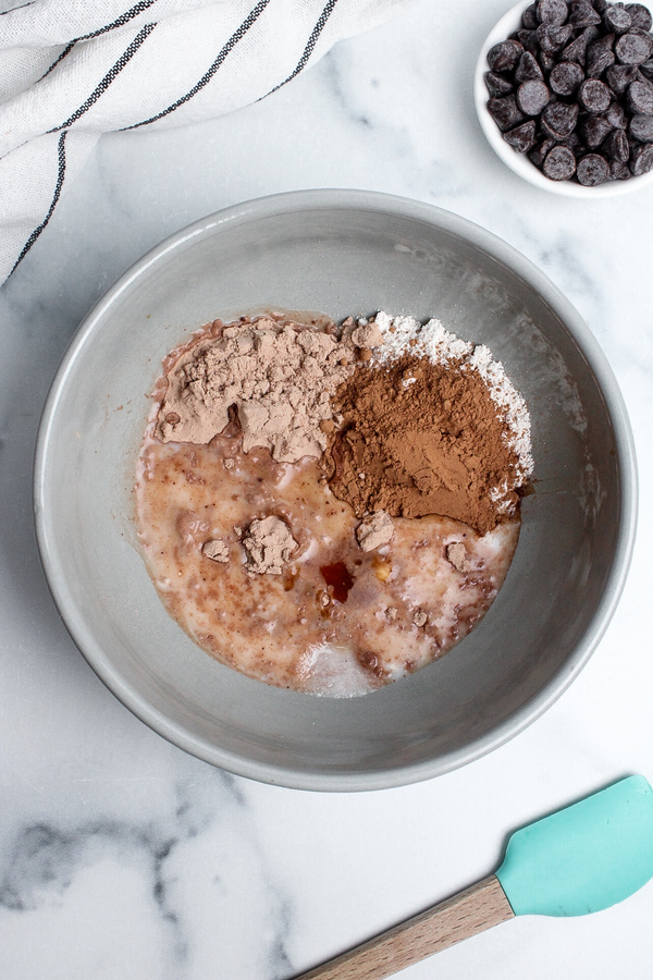 Oat flour, chocolate protein powder, cocoa powder, almond milk, almond butter, maple syrup, vanilla extract, and salt in a mixing bowl.
