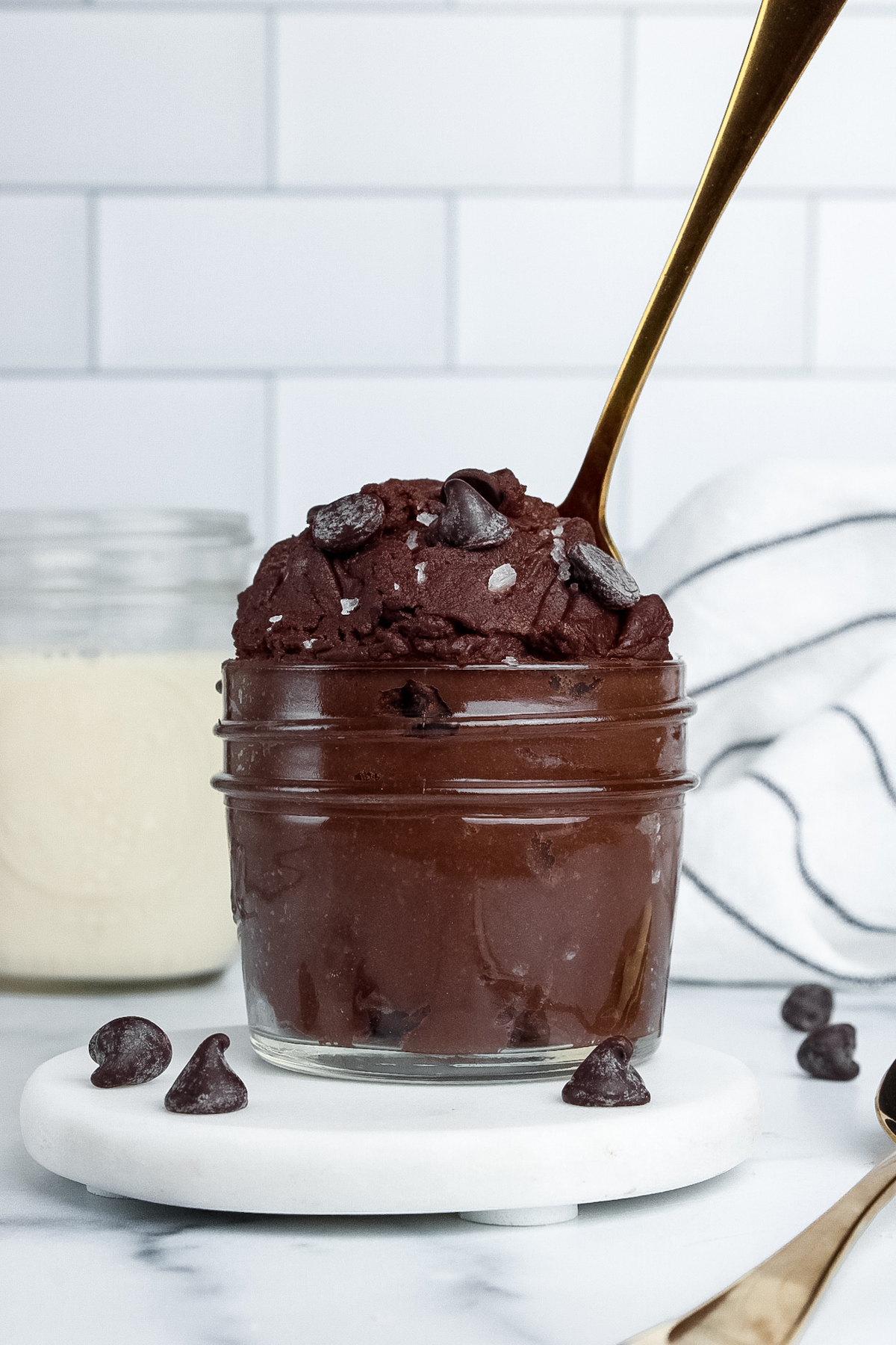 Jar of single-serve chocolate brownie batter served with a glass of non-dairy milk.
