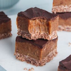 Two squares of no-bake double chocolate caramel slice stacked, with a bite taken out of one showing chocolate, caramel, and coconut layers.