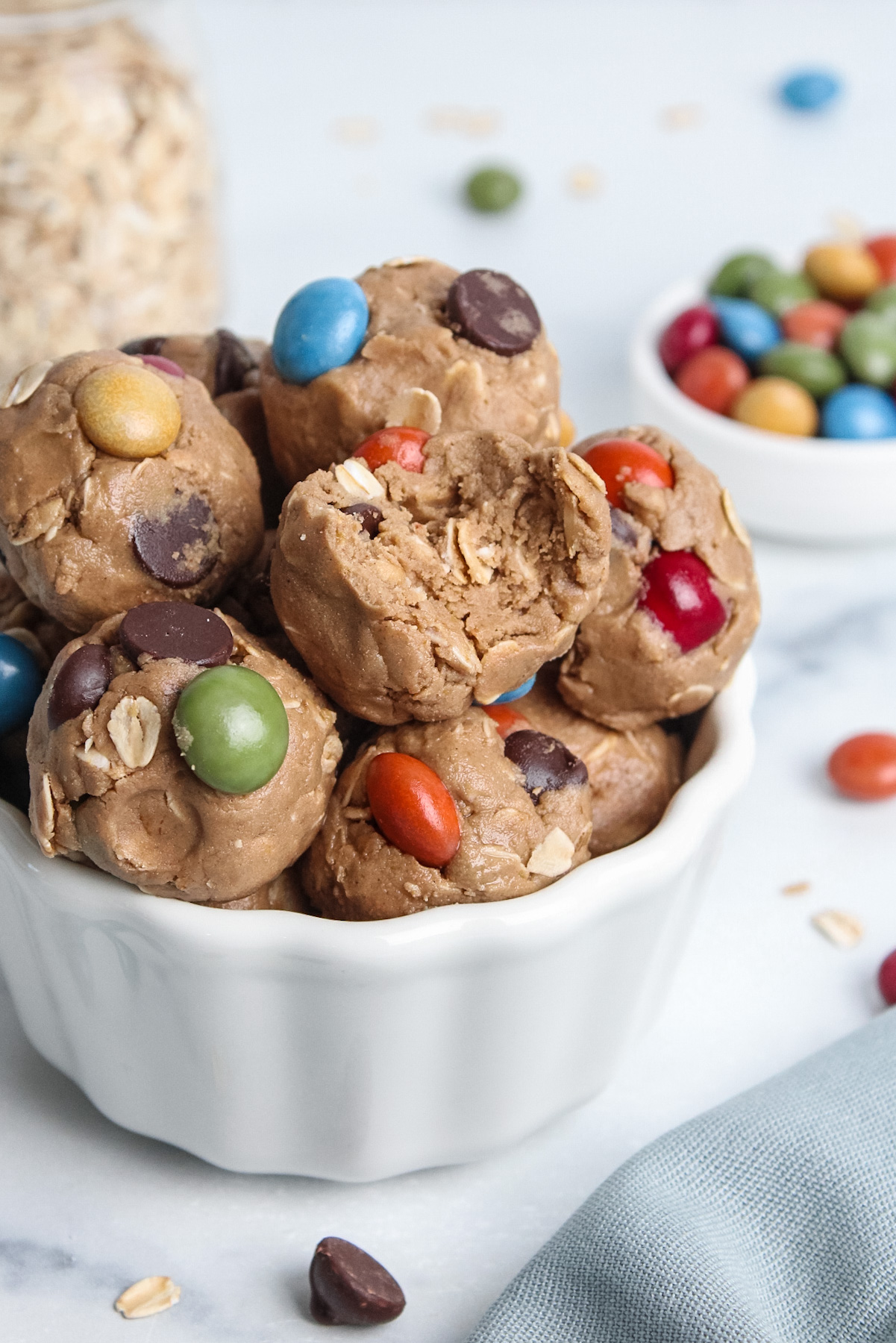Close-up of vegan monster cookie energy balls in a white bowl, with a bite showing the soft, chewy texture.