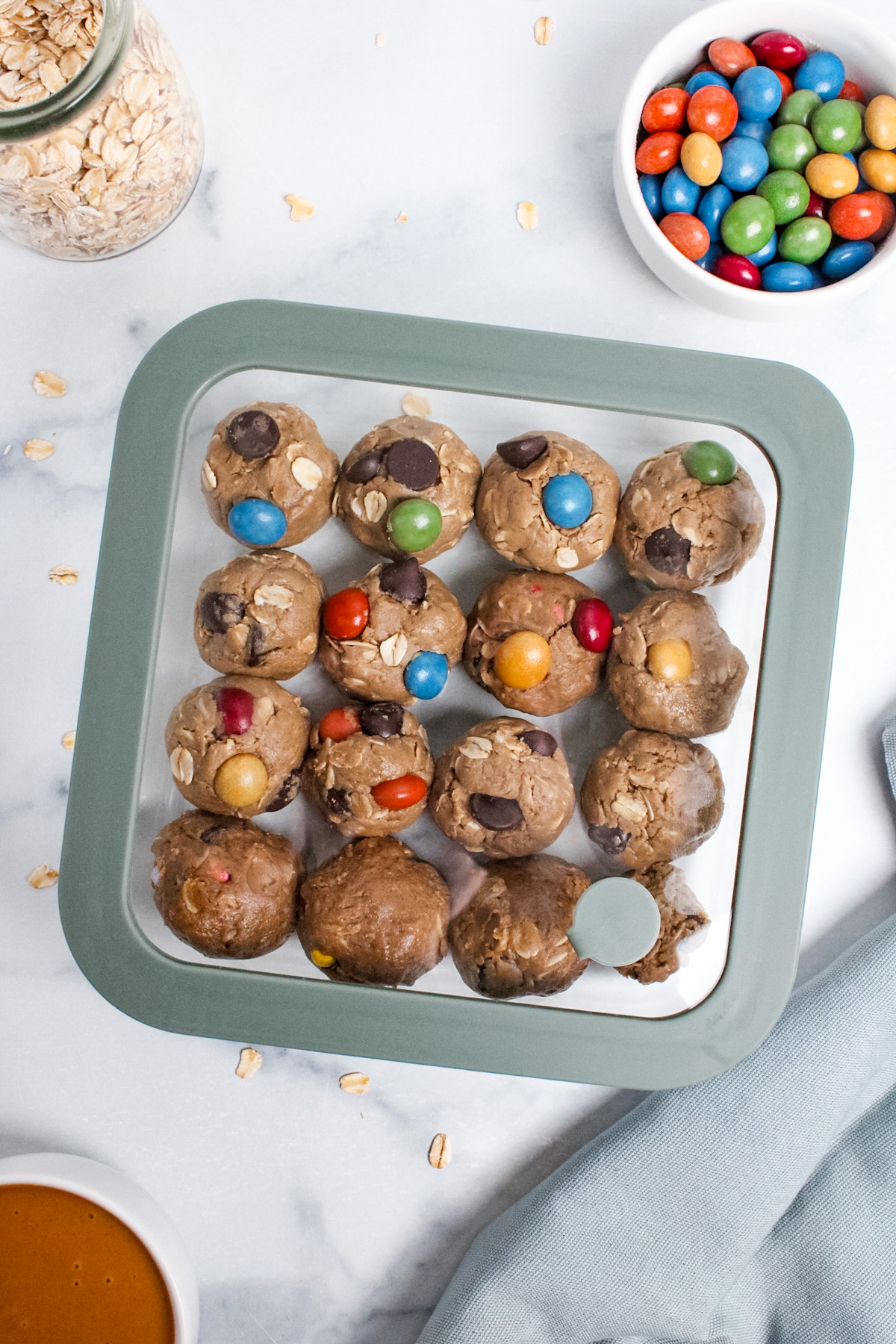 Batch of monster cookie energy balls in a clear glass container with a lid.