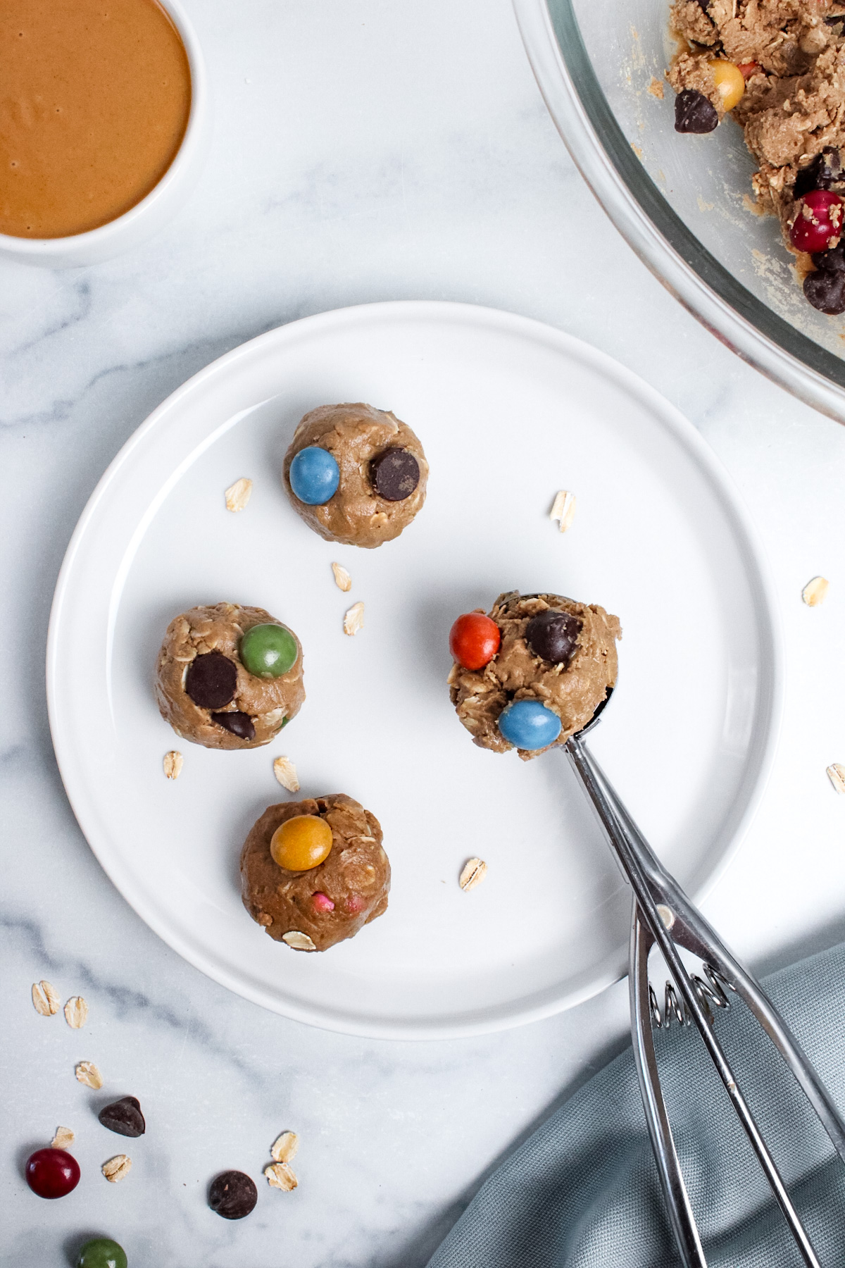 Scooping freshly rolled monster cookie energy balls with a cookie scoop onto a plate, showing their chocolate chip and candy-studded texture.