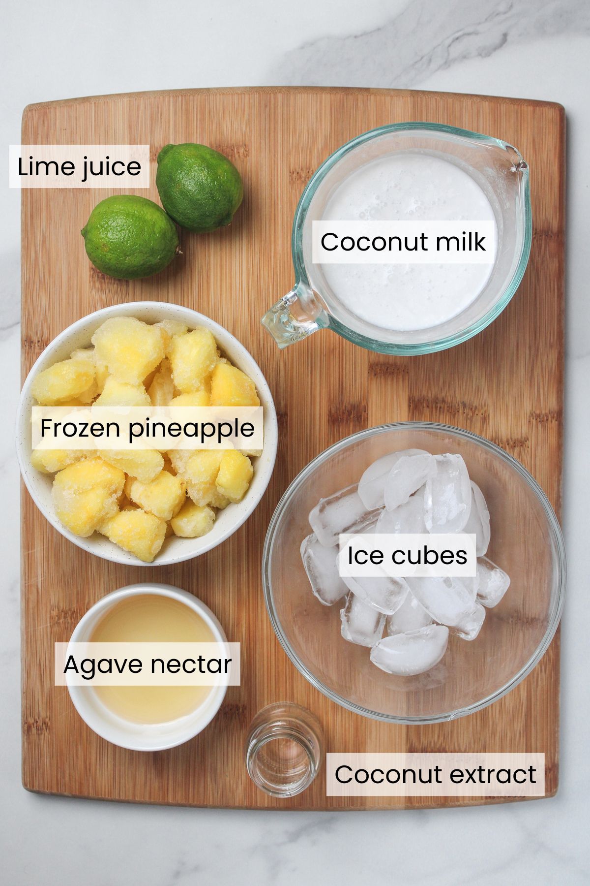 Ingredients for a healthy piña colada mocktail: lime juice, coconut milk, frozen pineapple, ice cubes, agave nectar, and coconut extract.