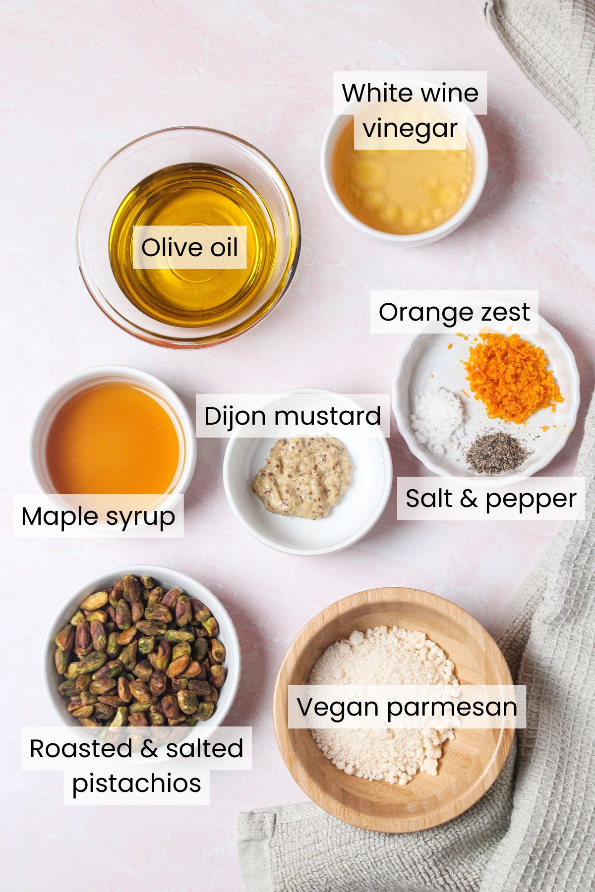 Ingredients for white wine vinaigrette: olive oil, white wine vinegar, orange zest, salt, pepper, dijon mustard, and maple syrup — alongside pistachios and vegan parmesan for the salad.