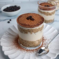 Tiramisu overnight oats in a glass, with layers of creamy coffee oats, non-dairy yogurt, and cocoa powder on top.
