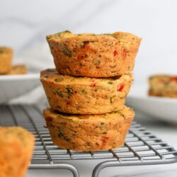 Stack of three savory vegan chickpea flour muffins with vegetables and vegan cheese, arranged on a wire rack.