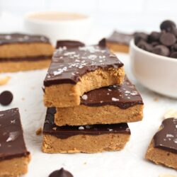 Stack of three chocolate peanut butter protein bars topped with flaky sea salt, with a bite taken out of one.