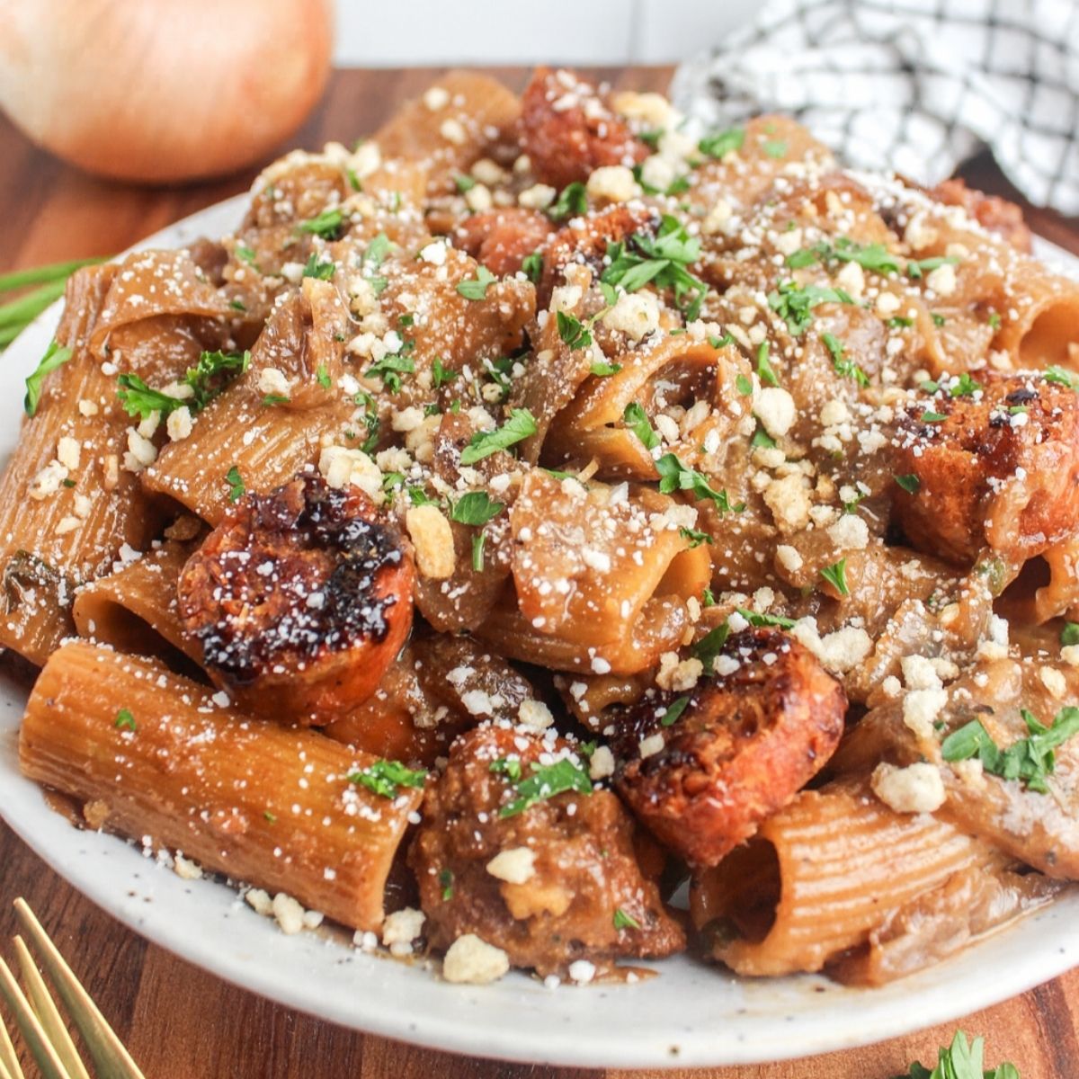 Plate of vegan French onion sausage pasta topped with breadcrumbs, vegan parmesan, and fresh parsley.