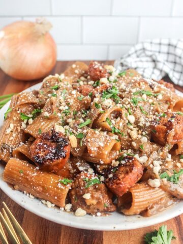 Plate of vegan French onion sausage pasta topped with breadcrumbs, vegan parmesan, and fresh parsley.