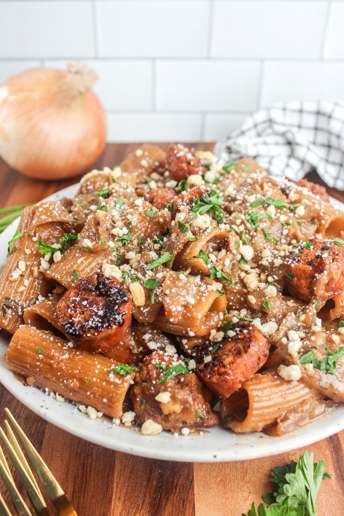 Plate of vegan French onion sausage pasta topped with breadcrumbs, vegan parmesan, and fresh parsley.