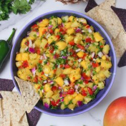 Overhead view of mango pineapple salsa in a bowl, with a tortilla chip dipping into it.