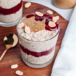 Peanut butter and jelly overnight oats in a glass, with a layer of raspberry jam in the middle and peanut butter, jam, and peanuts on top.