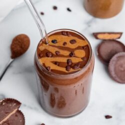Peanut butter cup smoothie in a glass with a straw, topped with a peanut butter drizzle and cacao nibs.