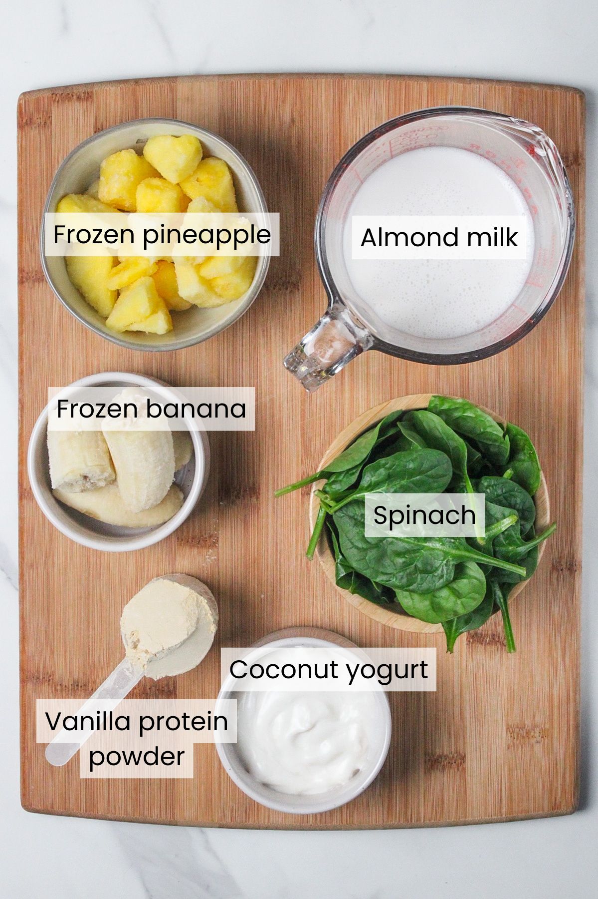 Ingredients needed to make a pineapple protein green smoothie: frozen pineapple, almond milk, frozen banana, spinach, vanilla protein powder, and coconut yogurt.