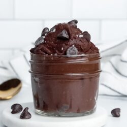 Single-serve vegan protein brownie batter in a jar, topped with chocolate chips and flaky sea salt.