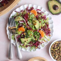 Overhead view of a colorful radicchio, orange, and pistachio salad on a plate with two forks.