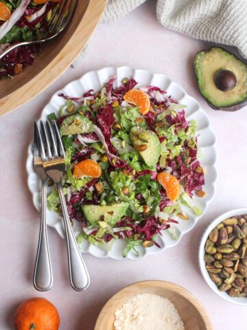 Overhead view of a colorful radicchio, orange, and pistachio salad on a plate with two forks.