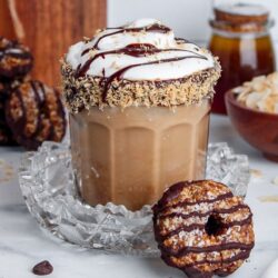 Iced Samoa Cookie Latte in a glass, topped with coconut whipped cream, chocolate syrup, and a toasted coconut rim.