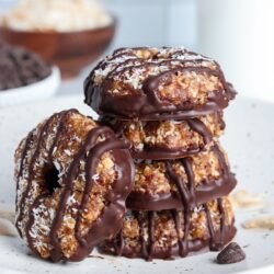 Stack of healthy no-bake Samoa cookies made with dates and toasted coconut, drizzled with chocolate, on a plate.