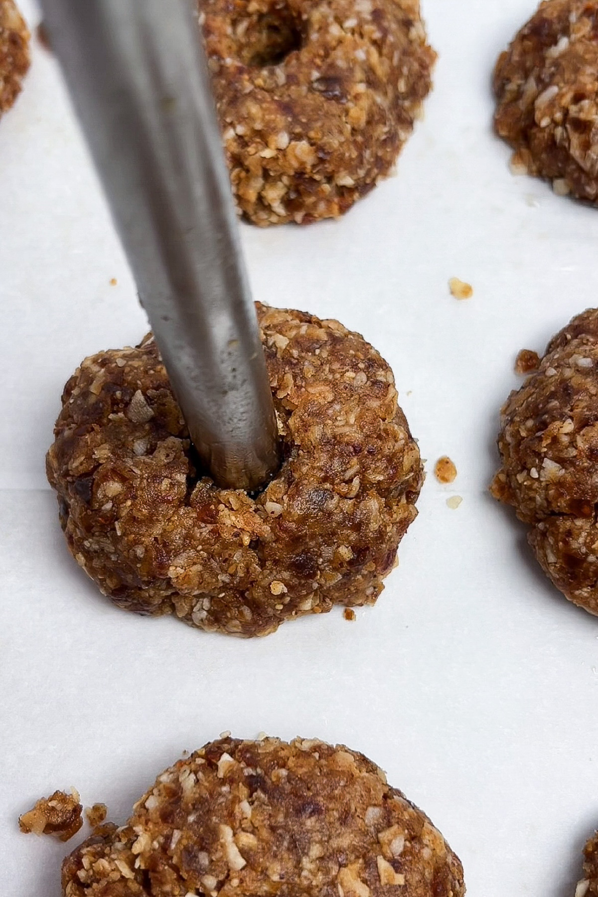 A straw poking a hole in the center of a flattened no-bake Samoa cookie on parchment paper.