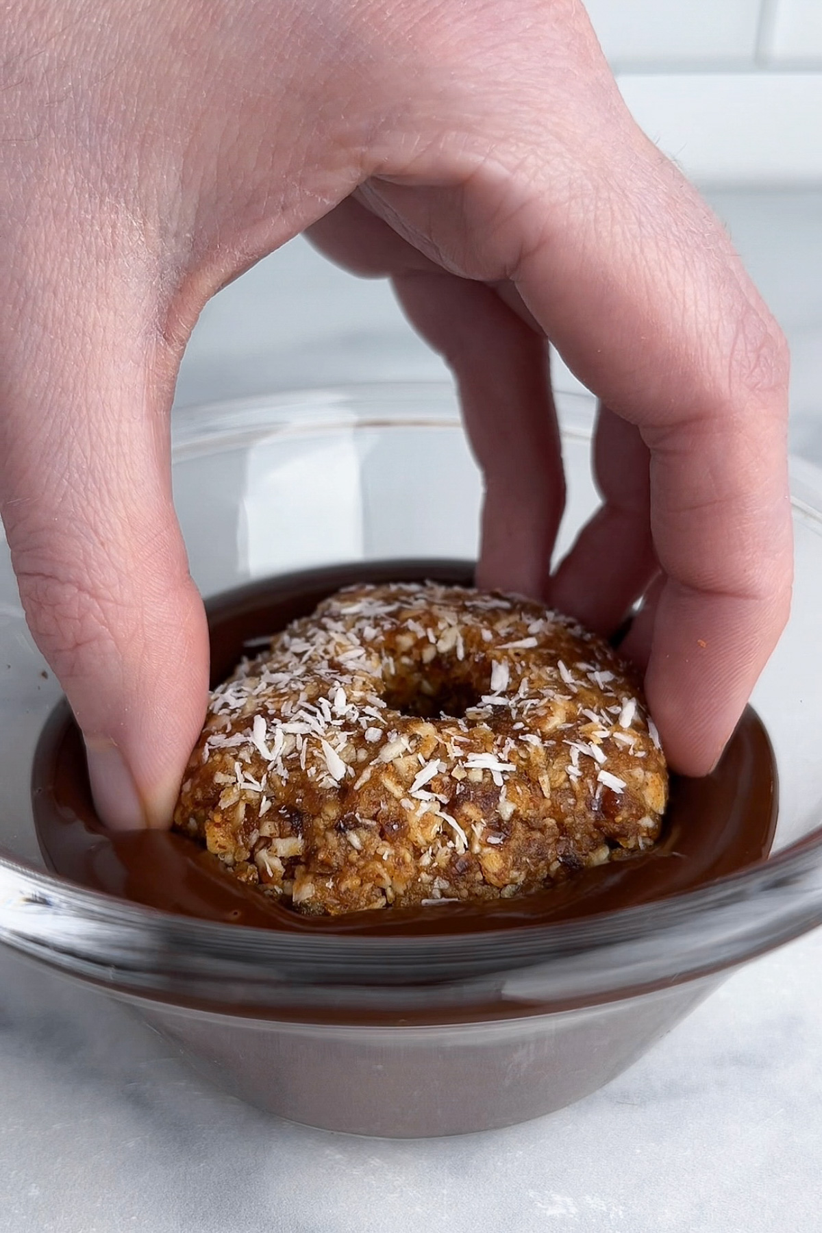 Hand dipping the bottom of a no-bake Samoa cookie into melted chocolate.