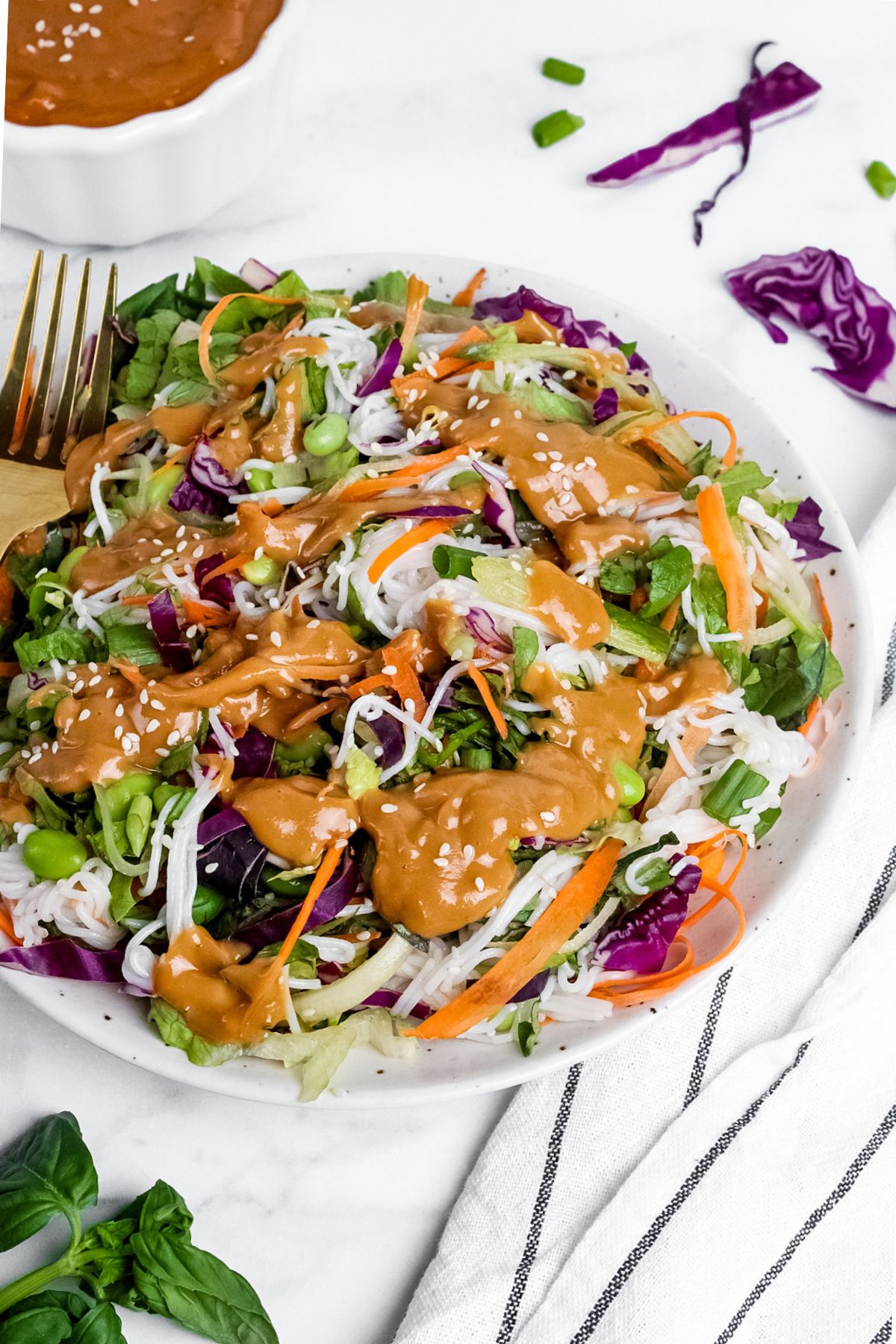 Angled view of a spring roll salad on a plate with a fork, drizzled with creamy peanut dressing.