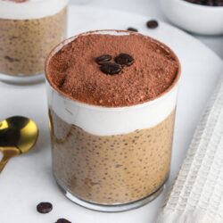Tiramisu chia pudding in a glass, with layers of coffee-flavored chia pudding, yogurt, and cocoa powder on top.