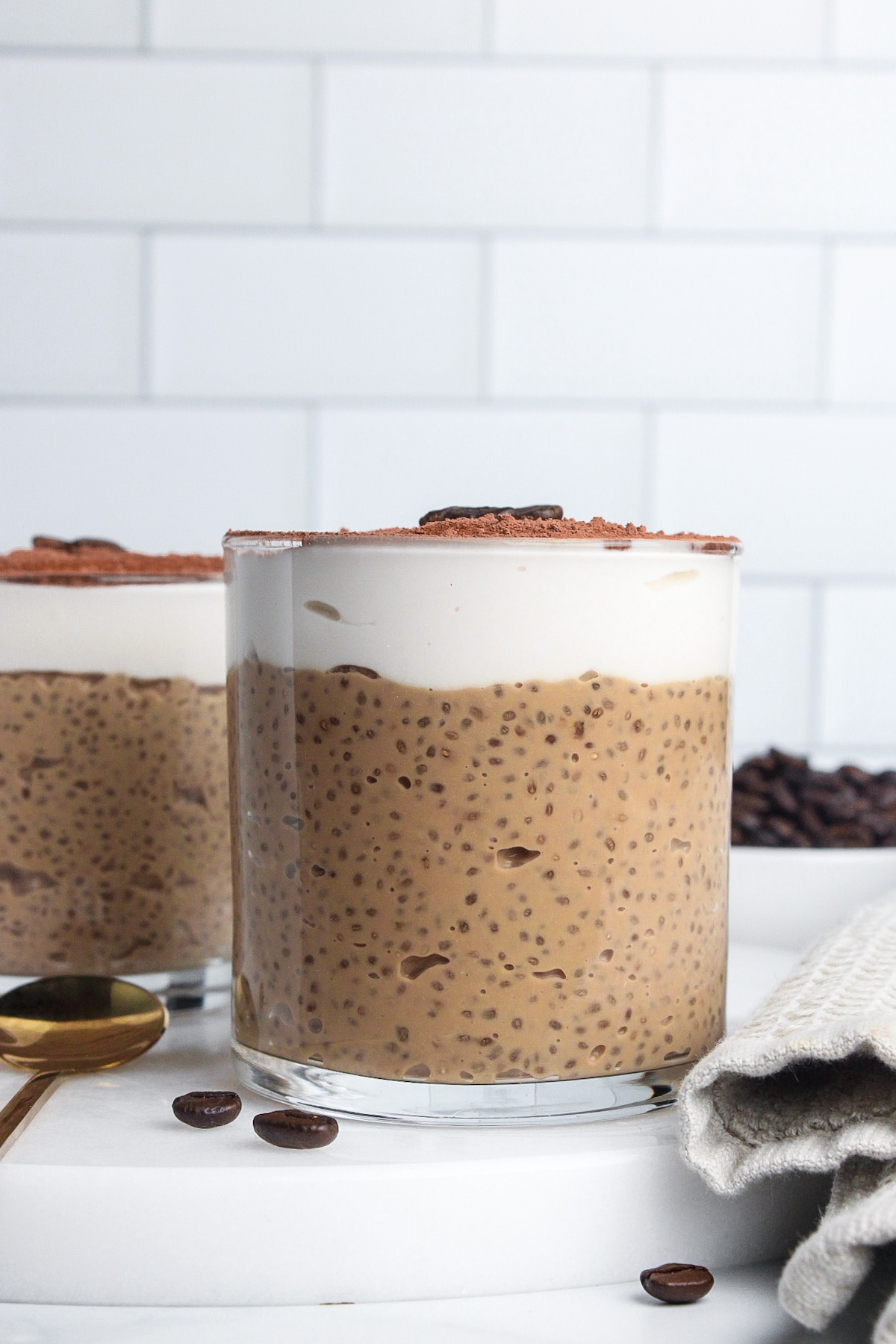 Straight-on view of two glasses of tiramisu chia pudding layered with yogurt and cocoa powder.