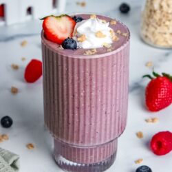 Berry pie smoothie in a glass, topped with whipped cream, granola, and fresh berries.