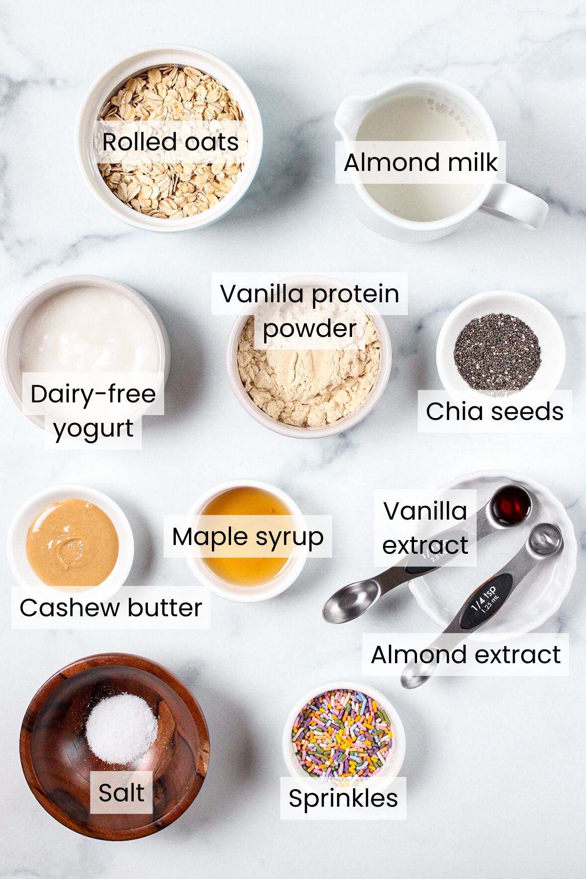 Ingredients for birthday cake overnight oats: rolled oats, almond milk, dairy-free yogurt, vanilla protein powder (optional), cashew butter, sprinkles, maple syrup, chia seeds, vanilla extract, almond extract, and salt.