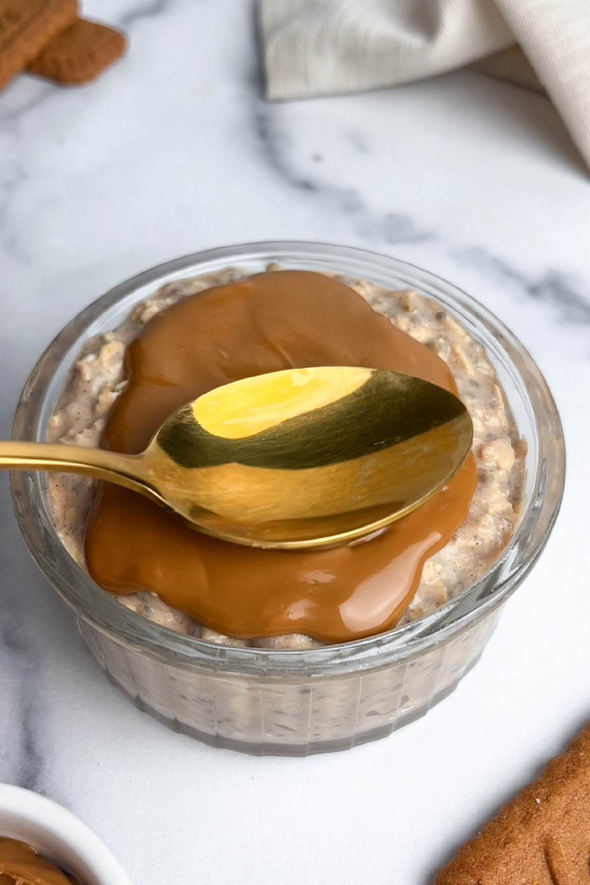 Overnight oats in a glass jar with melted Biscoff cookie butter being spread on top.
