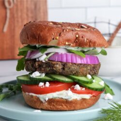 Loaded Mediterranean veggie burger on a plate with dairy-free tzatziki, vegan feta, and fresh vegetables.
