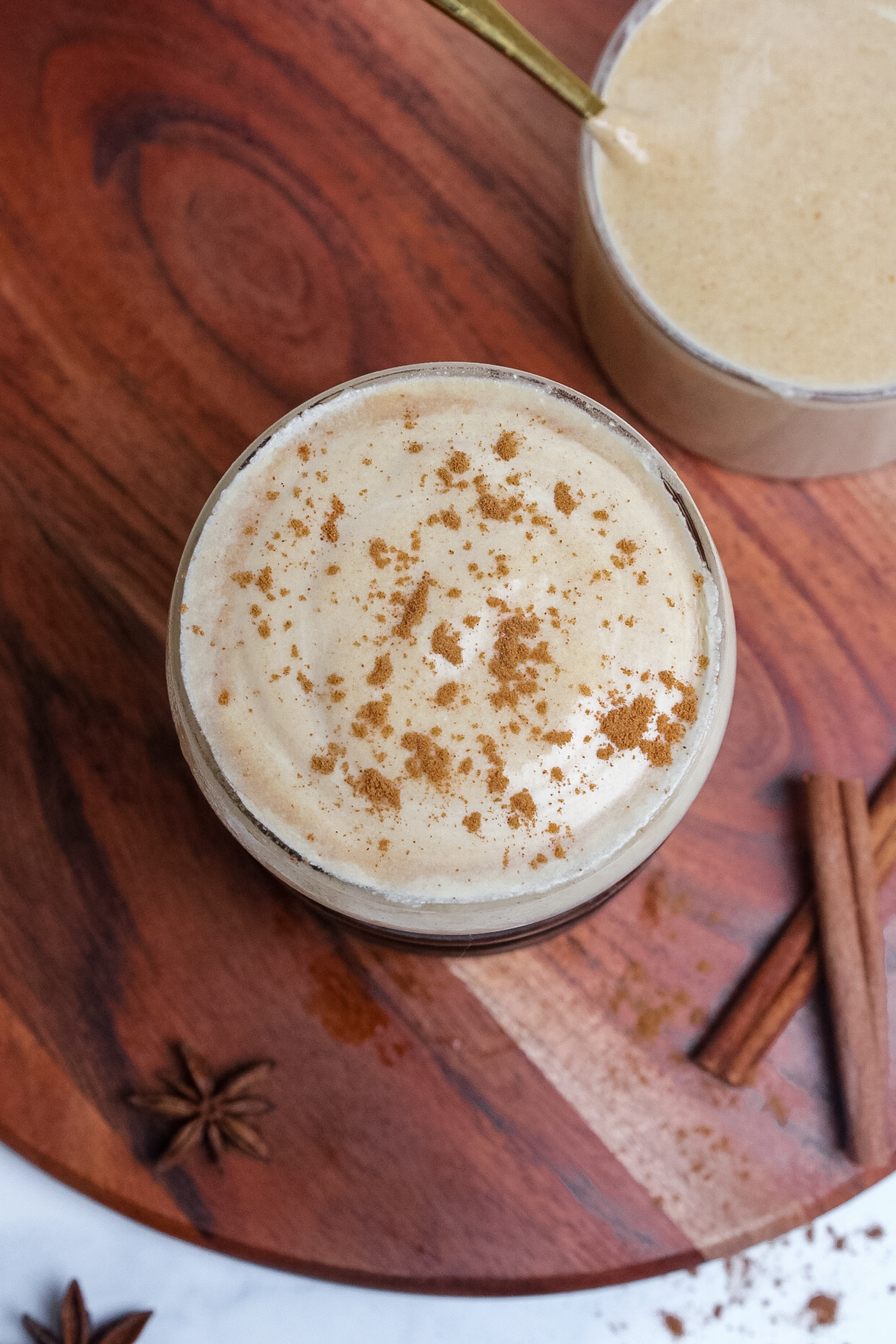 Overhead view of a glass of iced coffee topped with pumpkin cream cold foam, dusted with cinnamon.