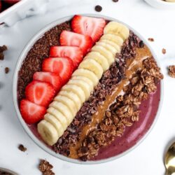 Strawberry banana espresso smoothie bowl topped with sliced strawberries, banana, granola, almond butter, and cacao nibs.