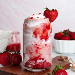 Strawberry glaze smoothie with coconut cream and strawberry swirls in a glass, garnished with a fresh strawberry.