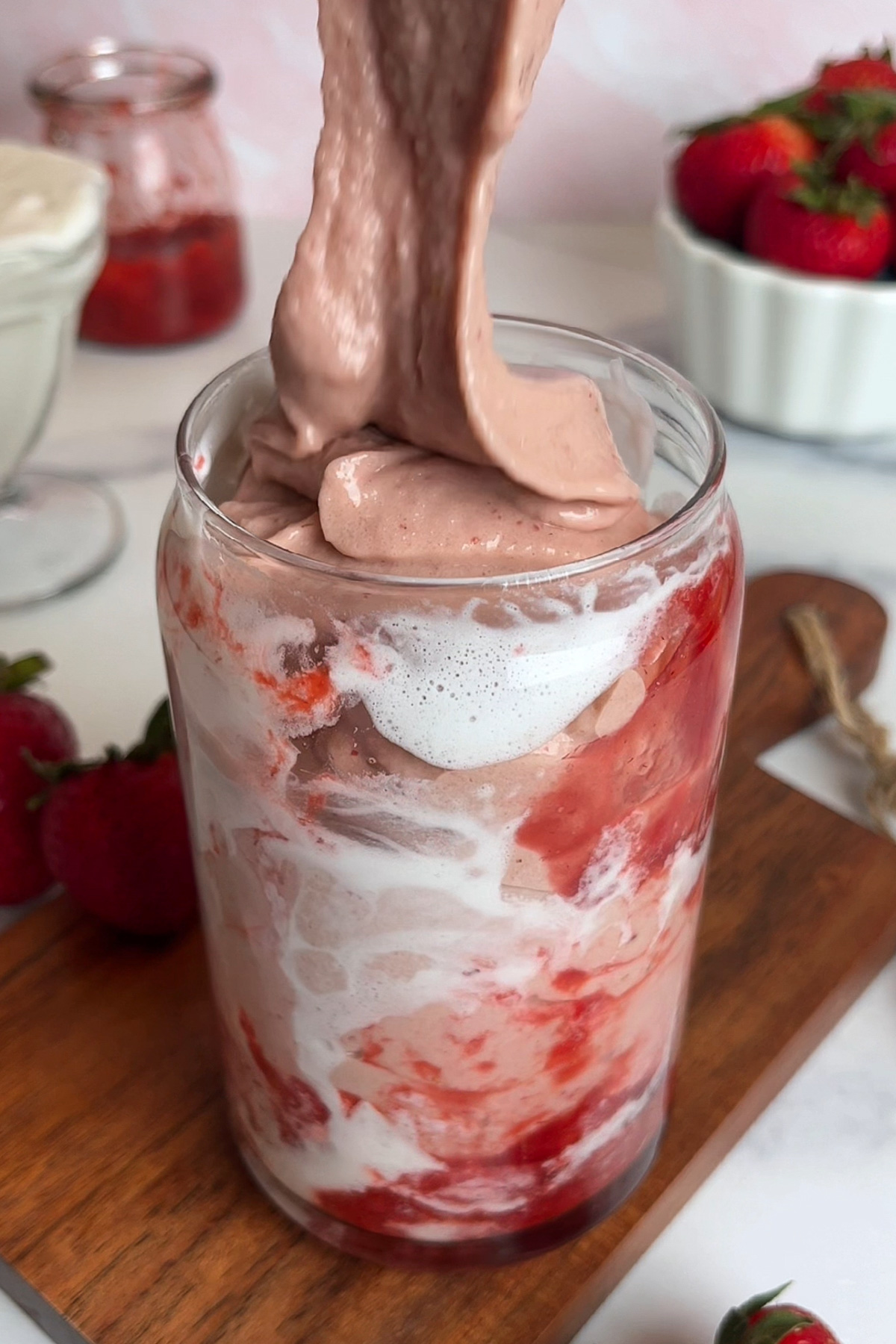 Strawberry glaze smoothie being poured into a glass lined with strawberry glaze and coconut cream.